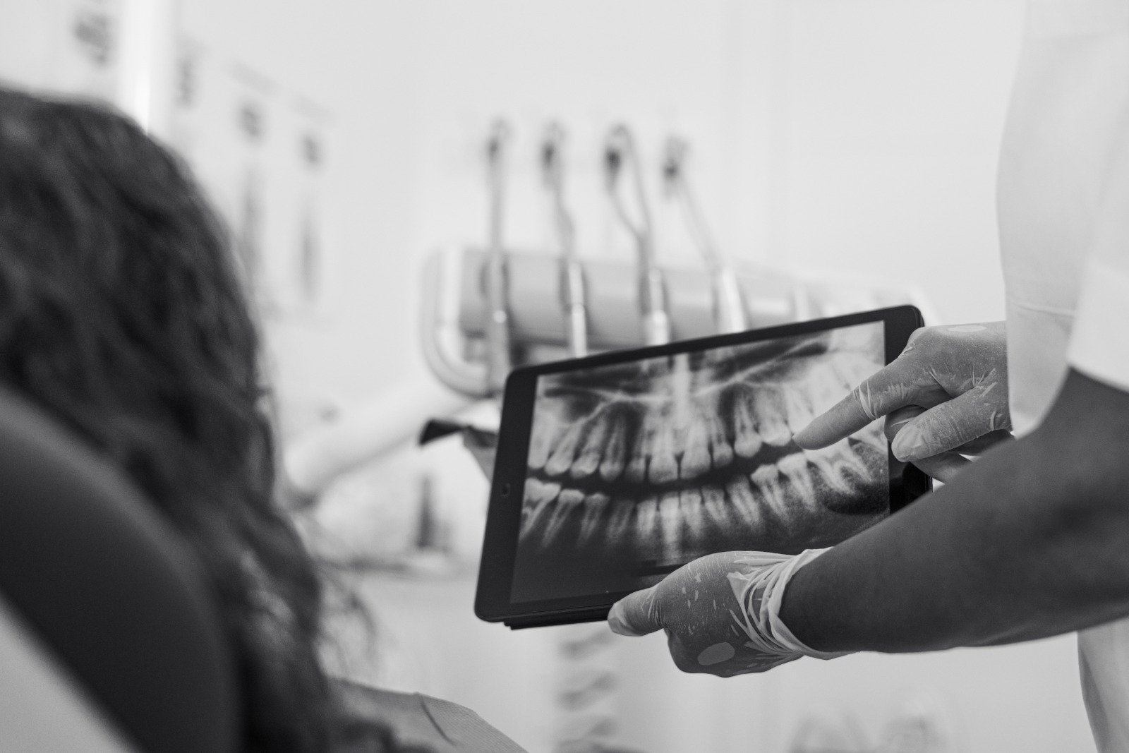 Fotografía en blanco y negro de una dentista mostrando una radiografía dental en una tableta a un paciente que está sentado de espaldas.