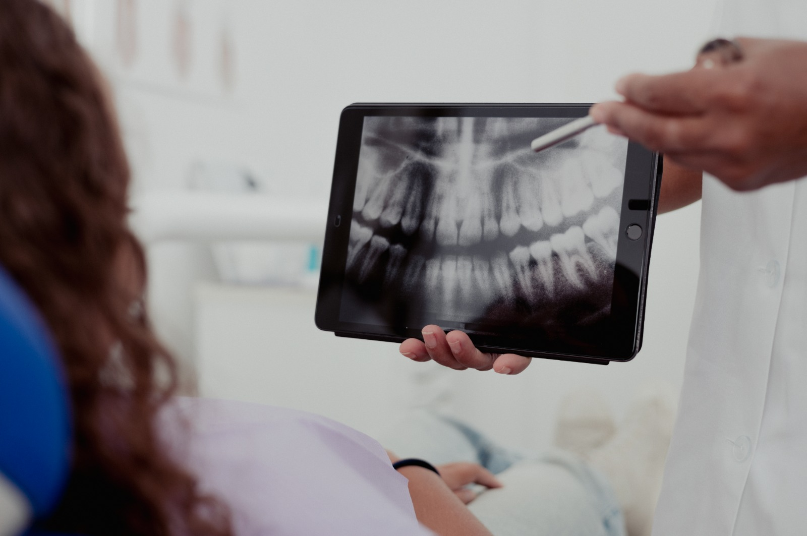 Fotografía a color de una dentista mostrando una radiografía dental en una tableta a un paciente que está sentado en una silla dental.